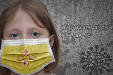 Little girl in medical mask with new mexico state flag stands near the old vintage wall with text coronavirus, covid, and virus picture. Stop virus concept