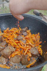 Cooking pilaf in a cauldron on the grill outside in the summer