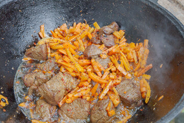 Cooking pilaf in a cauldron on the grill outside in the summer