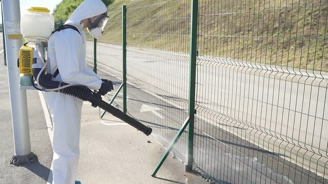Side view on hard-working man in hazard wearing with equipment for disinfection. Qutdoors.