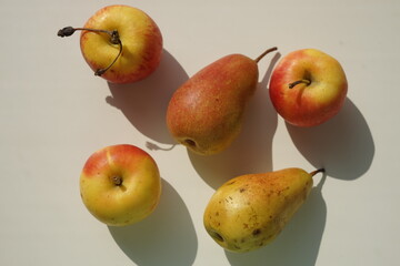Three yellow orange apples and two pears on a white sunny table.