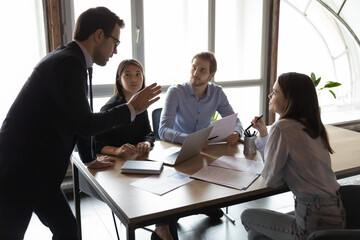 Skilled 30s confident male team leader in formal wear holding brainstorming meeting with interested...