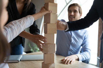 Close up focus on wooden blocks tower, built by happy teammates on office table. Young employees...