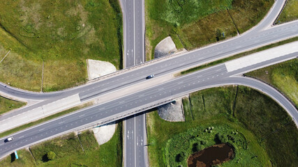 Top view of highway with intersection and roundabout in the middle of fields on a sunny day