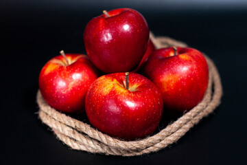 A pile of fresh red apples in the center of the screen. A jute rope is wrapped around the fruits. 