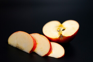 In the center of the screen are sliced slices and half of a red juicy Apple. Dark background. 