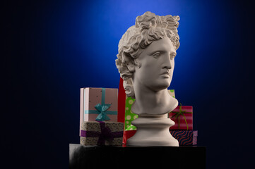Statue of Apollo Belvedere in a red cap of Santa Claus, gifts boxes and packages, in blue contour light on multi-colored backgrounds. Composition for congratulations.