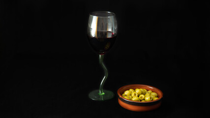 Glass of red wine and green olives, aperitif, on black background	