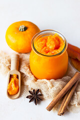 Canned organic pumpkin puree in glass jar with fresh pumpkin, cinnamon and anise on light stone background. Ingredient for Thanksgiving, autumn or winter recipes.