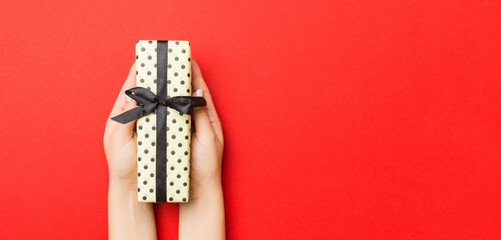 Female's hands holding striped gift box with colored ribbon on red background. Christmas concept or other holiday handmade present box, concept top view with copy space