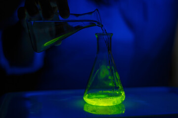 A researcher experimenting with a green fluorescent material reaction in a glass conical flask in dark biochemistry laboratory for health