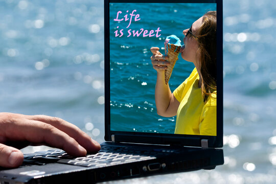 Laptop with picture of girl eating ice cream cone on its monitor in front of blue sea 