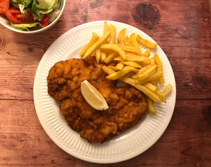 Wiener Schnitzel with french fries  and lemon. Viennese breaded Escalope, coated in flour, egg and breadcrumbs, then deep fried to golden brown and served with french fries, salad and lemon.