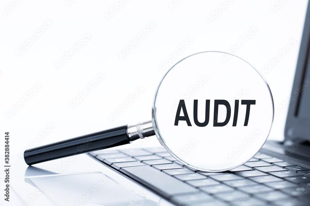 Poster text audit on a magnifying glass lying on the keyboard of a laptop