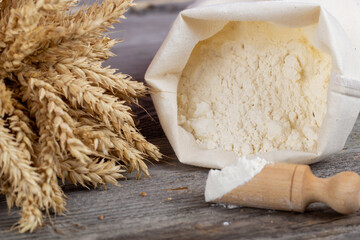 Flour sack, ears and wooden measuring cup on wooden background.