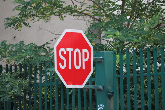 stop sign shown diagonally from the side in front of a green fence and tree