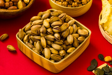 Fresh,crispy pistachio nuts in wooden bowl on vivid red background with other nuts