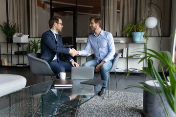 Happy two male partners shaking hands, making agreement after negotiations in modern office....