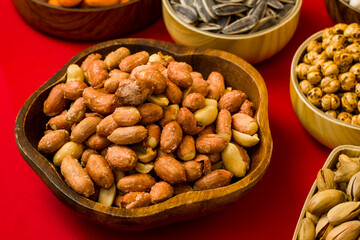 Fresh roasted salted peanuts in wooden bowl on red surface with other nuts.