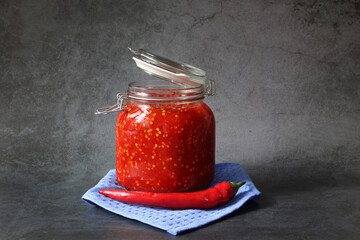 Ground hot red pepper with tomatoes in a glass jar on a dark background. A spicy seasoning made from pepper and tomatoes at home. Home cooking.