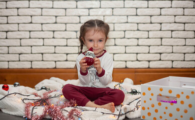 A little girl looks at the camera and Christmas decorations and New Year's garlands are laid out around her. A girl holding a Christmas tree toy rat, a symbol of the outgoing year. Christmas holidays.