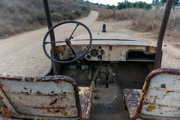 Old 1928 jeep body rusted seats and dashboard while broken down along the side of hiking trail.