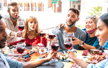 Friends toasting red wine at restaurant bar wearing opened face masks - New normal lifestyle...
