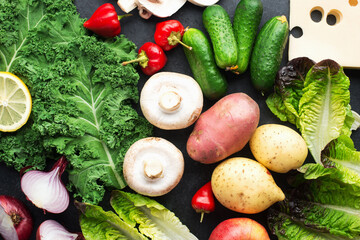 Healthy simple home food ingredients farm vegetables potatoes, cucumbers, cabbage, kale, garlic, onions, mushrooms, cheese, lettuce, hot peppers on a dark background. Balanced diet ready concept