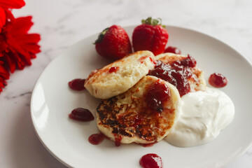Tasty cheese pancakes with strawberries, sour cream and lingonberry jam. Cheese pancakes on a plate