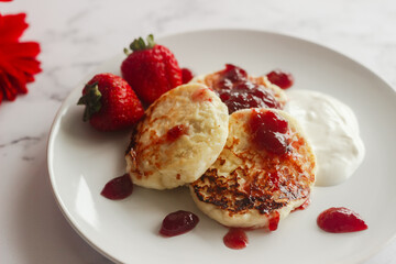 Tasty cheese pancakes with strawberries, sour cream and lingonberry jam. Cheese pancakes on a plate
