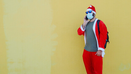 Man dressed as Santa Claus with medical mask and sunglasses talking with the smartphone. Funny santa claus, christmas and coronavirus	