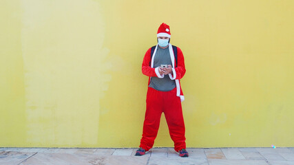 Man dressed of Santa Claus with medical mask and sunglasses chatting with the smartphone. Funny santa claus, christmas and coronavirus