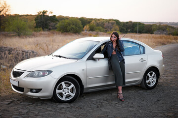 a brunette girl in a leather jacket and black trousers near the car