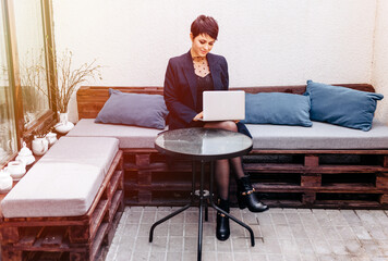 Young attractive businesswoman sitting in a coffee shop terrace with her laptop, working remotely, freelance worker