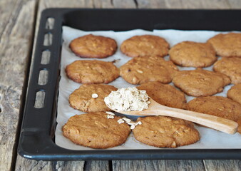Homemade oatmeal cookies on a baking sheet from the kitchen oven, with cereal in a spoon on a wooden background.Diet healthy food.