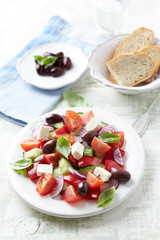 Simple salad with cherry tomatoes, feta cheese, kalamata olives, red pepper and fresh herbs. Bright wooden background. Close up.	