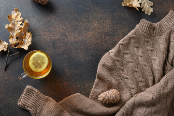 Fototapeta na wymiar Warming tea with lemon in cozy lifestyle with fall leaves and cozy scarf on brown background. View from above with copy space.