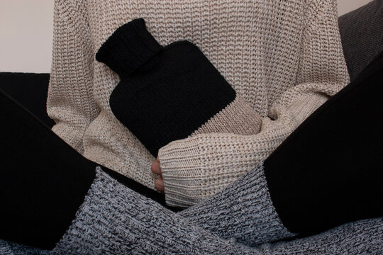 Frau in Strickpullover und Wollsocken mit einer W&auml;rmflasche