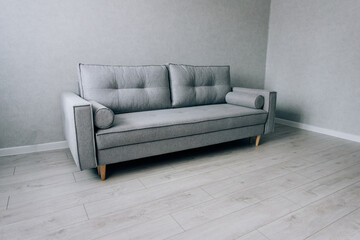 Modern grey sofa with wooden legs in the room