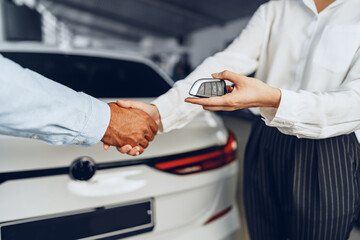 Car seller and buyer handshake at car dealership against a new car