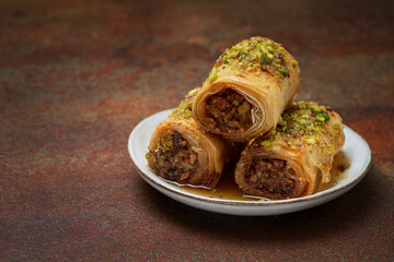 Rolled baklawa, home made traditional dessert, baqlawa, baqlava, baklava on dark surface, selective focus. Ramadan iftar food concept with rosary. Space for text.