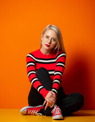 Style hipster girl sitting on a floor near orange background