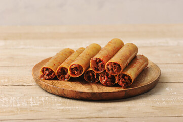 Cannelloni stuffed with minced meat with tomatoes before cooking.  Cannelloni on a wooden plate. Light wooden background.