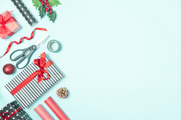 Gift boxes wrapped in black and white striped and red paper with wrapping materials over a blue background. Christmas presents preparation. Copy space.