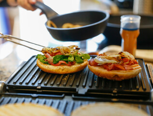 Woman cooking bacon and cheese burgers at home