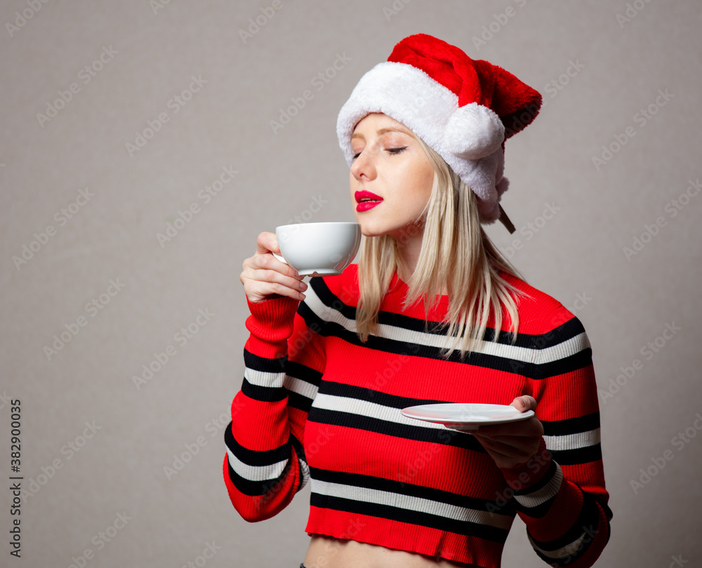 Poster smiling girl in christmas hat with cup of coffee on grey background