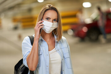 Adult woman in protection mask using cellphone in underground parking lot