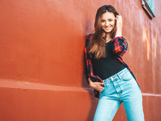 Portrait of beautiful smiling model. Female dressed in summer hipster checkered shirt and jeans. She posing near wall in the street. Funny and positive woman having fun outdoors