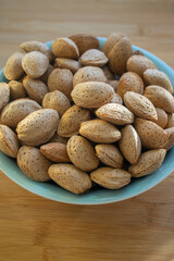 Almonds on table in hard nutshells, group of dry ripened fruits in blue bowl, crop food ingredients ready for cooking