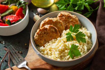 Healthy vegan food. Red fish cutlets with bulgur and fresh vegetable salad on a dark stone or slate table.